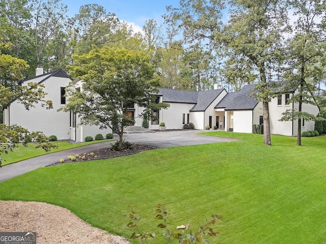modern inspired farmhouse featuring stucco siding, a chimney, aphalt driveway, a front lawn, and roof with shingles