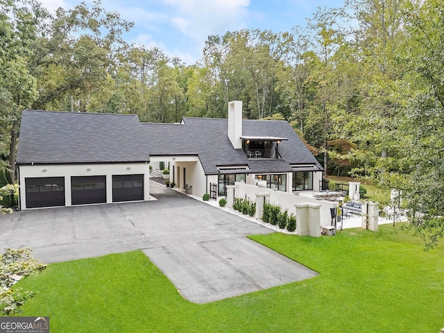rear view of property featuring a lawn, a chimney, aphalt driveway, a garage, and roof with shingles