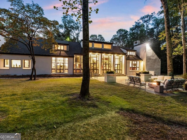 back of house at dusk with a yard, stucco siding, a patio area, and an outdoor living space
