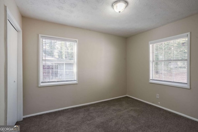 unfurnished room with dark colored carpet and a textured ceiling