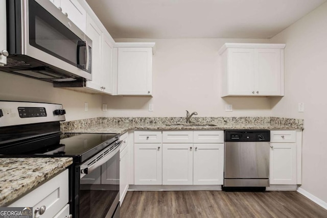 kitchen with appliances with stainless steel finishes, hardwood / wood-style floors, white cabinetry, sink, and light stone countertops