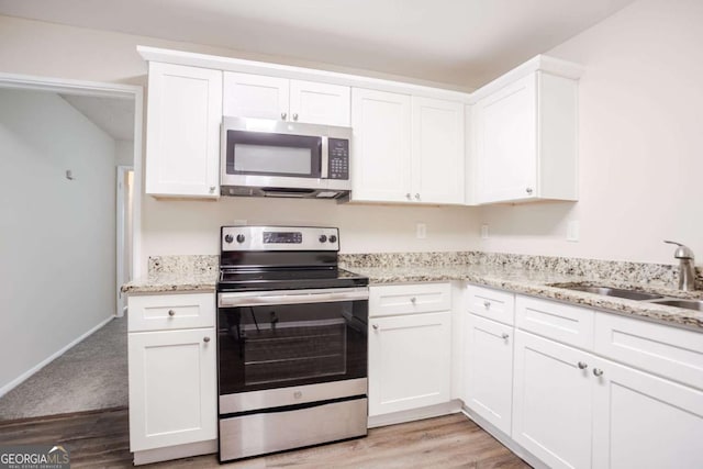 kitchen with sink, white cabinetry, stainless steel appliances, light stone countertops, and light hardwood / wood-style floors