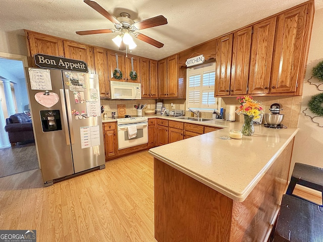 kitchen with white appliances, light hardwood / wood-style flooring, a breakfast bar, a textured ceiling, and kitchen peninsula