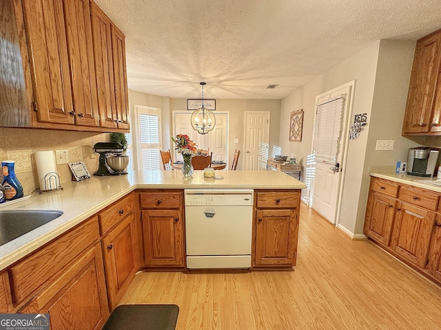 kitchen featuring pendant lighting, white dishwasher, tasteful backsplash, kitchen peninsula, and light wood-type flooring