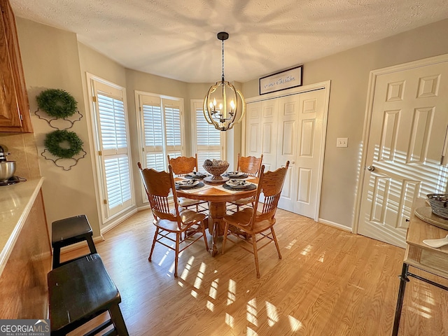 dining area with an inviting chandelier, light hardwood / wood-style flooring, and a textured ceiling