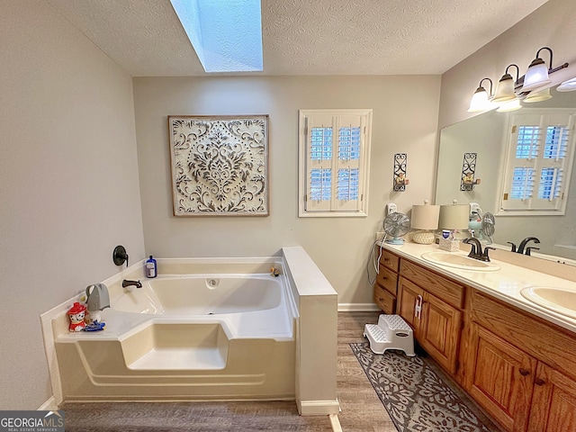 bathroom with a skylight, vanity, wood-type flooring, a textured ceiling, and a bathing tub