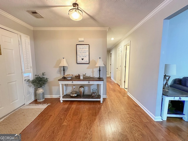 foyer entrance featuring hardwood / wood-style floors, ornamental molding, and a textured ceiling