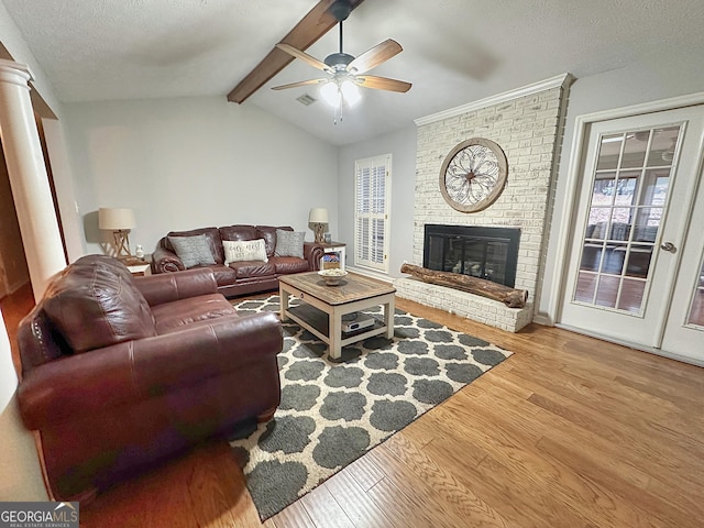 living room featuring a fireplace, lofted ceiling with beams, ceiling fan, light hardwood / wood-style floors, and a textured ceiling