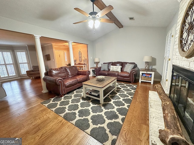 living room with lofted ceiling with beams, dark hardwood / wood-style flooring, ceiling fan, a fireplace, and decorative columns