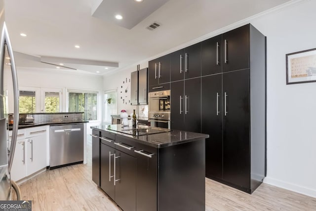 kitchen with dark stone countertops, a kitchen island, light hardwood / wood-style flooring, and appliances with stainless steel finishes