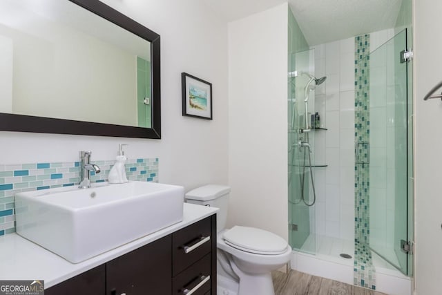 bathroom featuring hardwood / wood-style flooring, vanity, decorative backsplash, a shower with shower door, and toilet