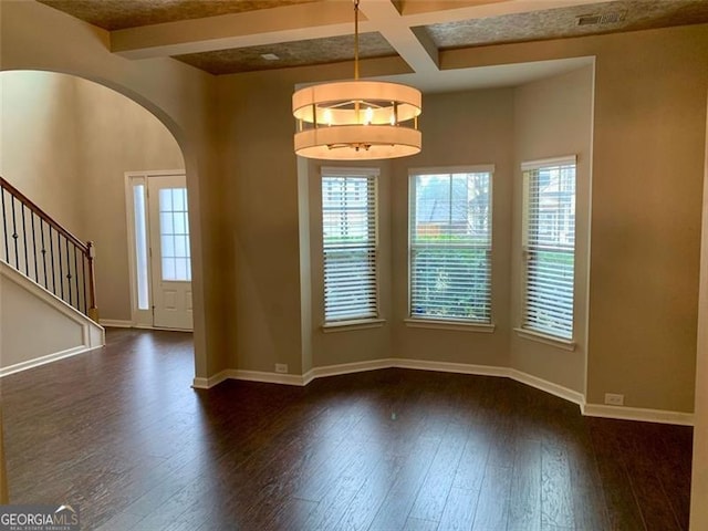 unfurnished room featuring coffered ceiling, beam ceiling, dark wood-type flooring, and a wealth of natural light