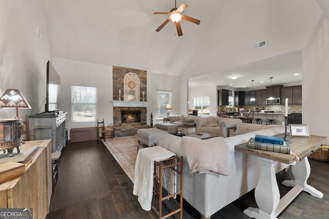 living room featuring ceiling fan, a stone fireplace, dark hardwood / wood-style floors, and high vaulted ceiling