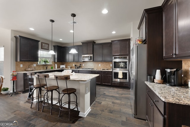 kitchen with decorative light fixtures, a breakfast bar area, decorative backsplash, a center island, and stainless steel appliances