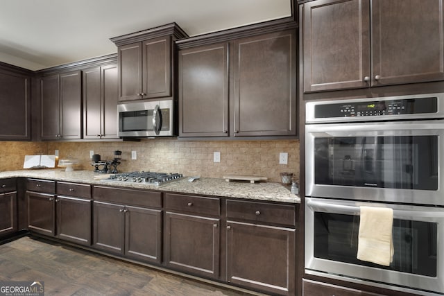 kitchen with appliances with stainless steel finishes, dark hardwood / wood-style floors, tasteful backsplash, light stone counters, and dark brown cabinetry