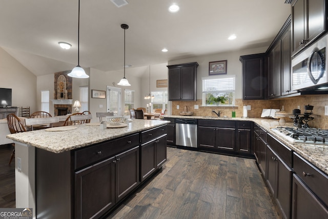 kitchen featuring sink, hanging light fixtures, stainless steel appliances, a center island, and a stone fireplace