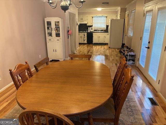 dining space featuring crown molding, french doors, a chandelier, and light wood-type flooring