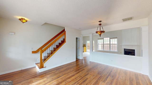 unfurnished living room with decorative columns, hardwood / wood-style floors, and a textured ceiling