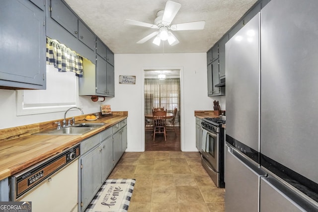 kitchen with butcher block counters, sink, ceiling fan, stainless steel appliances, and wall chimney range hood