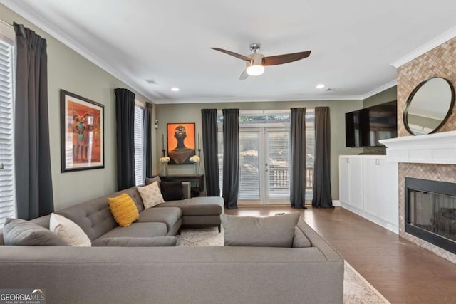 living room featuring ceiling fan, ornamental molding, a fireplace, and wood-type flooring