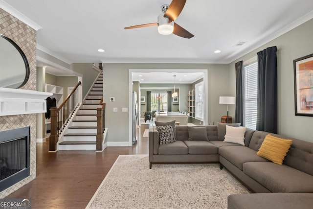 living room with crown molding, ceiling fan, dark hardwood / wood-style floors, and a tiled fireplace