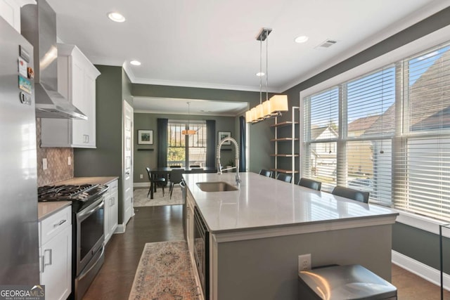 kitchen with sink, hanging light fixtures, appliances with stainless steel finishes, a kitchen island with sink, and white cabinets