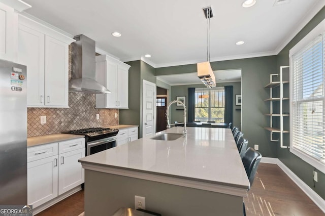 kitchen featuring white cabinetry, stainless steel appliances, decorative light fixtures, and wall chimney range hood