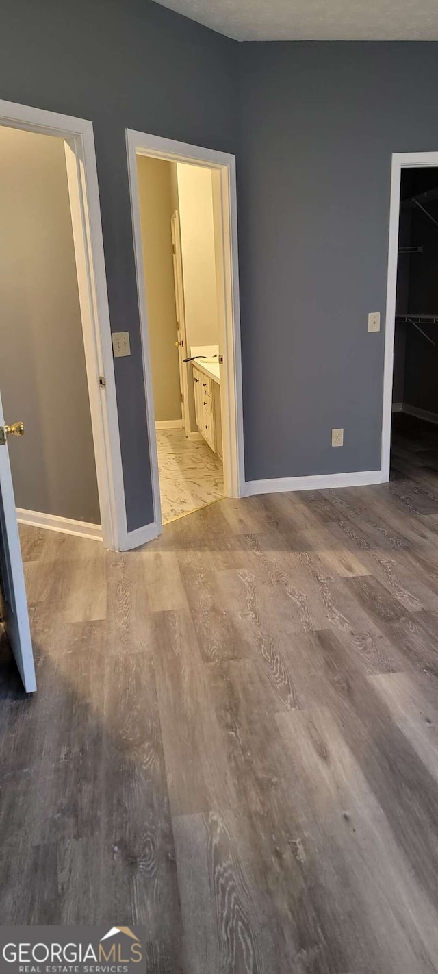 unfurnished bedroom featuring hardwood / wood-style flooring, ensuite bathroom, and a spacious closet