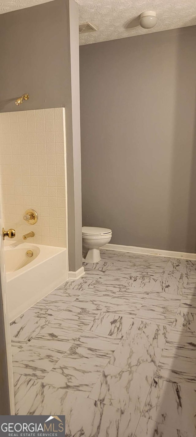 bathroom with a bathing tub, a textured ceiling, and toilet