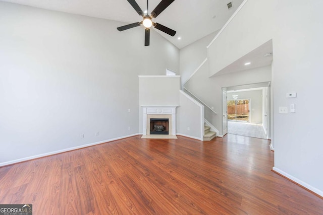 unfurnished living room featuring hardwood / wood-style flooring, a towering ceiling, and ceiling fan