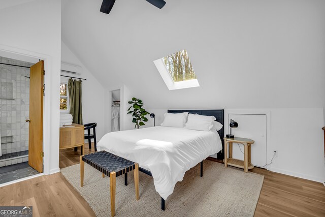 bedroom with wood-type flooring, a wall mounted air conditioner, vaulted ceiling with skylight, and ceiling fan