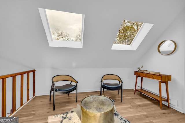 sitting room featuring vaulted ceiling with skylight and light wood-type flooring