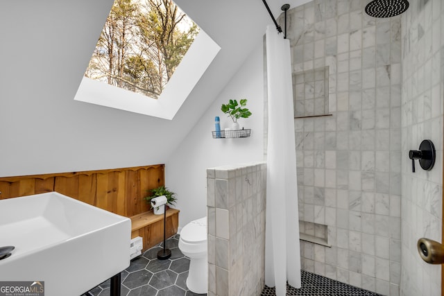 bathroom with vaulted ceiling with skylight, sink, tile patterned flooring, tiled shower, and toilet