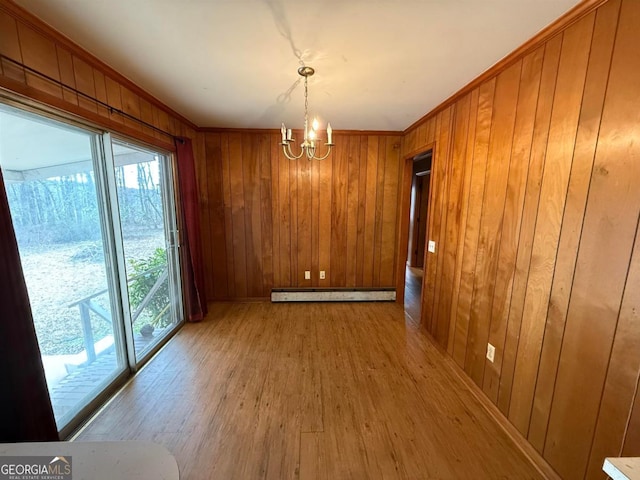 unfurnished dining area featuring an inviting chandelier, a baseboard heating unit, ornamental molding, light hardwood / wood-style floors, and wood walls