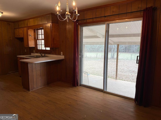 kitchen with sink, hardwood / wood-style flooring, hanging light fixtures, wooden walls, and kitchen peninsula