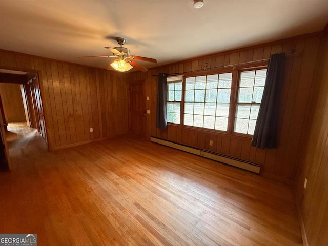 unfurnished room with wooden walls, baseboard heating, and light hardwood / wood-style floors