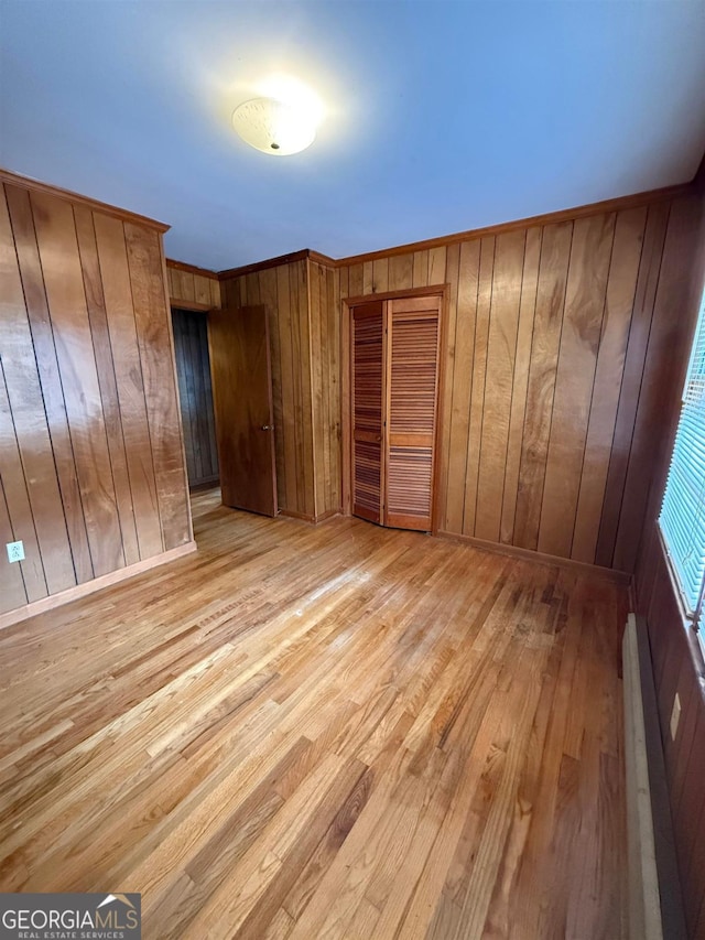 unfurnished bedroom with a baseboard radiator, ornamental molding, light hardwood / wood-style floors, and wood walls