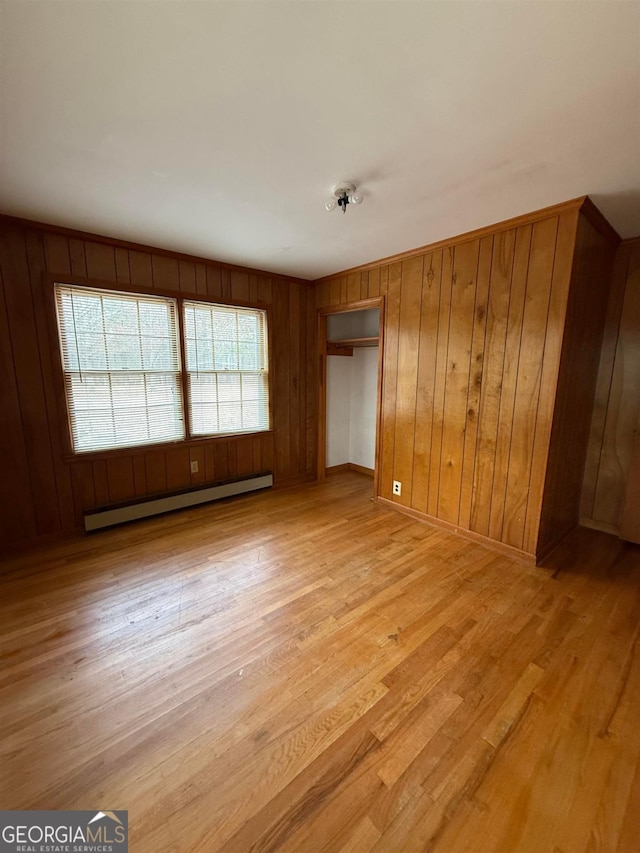 interior space featuring a baseboard radiator, wooden walls, a closet, and light wood-type flooring