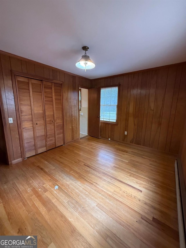 unfurnished bedroom with wooden walls, a closet, ceiling fan, light hardwood / wood-style floors, and a baseboard heating unit