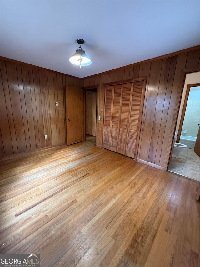 unfurnished bedroom featuring connected bathroom, light hardwood / wood-style flooring, wooden walls, and multiple closets