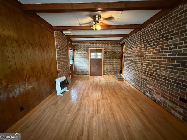 unfurnished living room featuring ceiling fan, hardwood / wood-style floors, heating unit, brick wall, and beamed ceiling