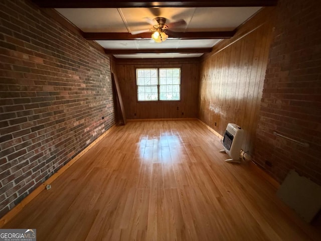 empty room featuring beamed ceiling, brick wall, heating unit, and light hardwood / wood-style flooring