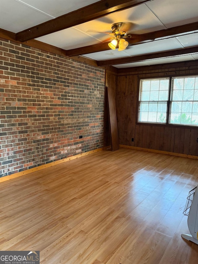 spare room featuring beam ceiling, light hardwood / wood-style floors, and brick wall