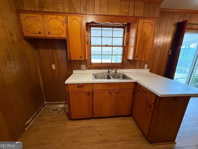 kitchen with sink, light wood-type flooring, kitchen peninsula, and wood walls