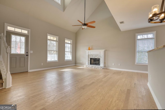 unfurnished living room with high vaulted ceiling, a wealth of natural light, a fireplace, and light hardwood / wood-style floors