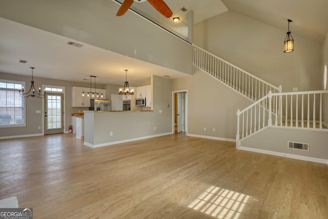 unfurnished living room with ceiling fan with notable chandelier, light hardwood / wood-style floors, and a high ceiling