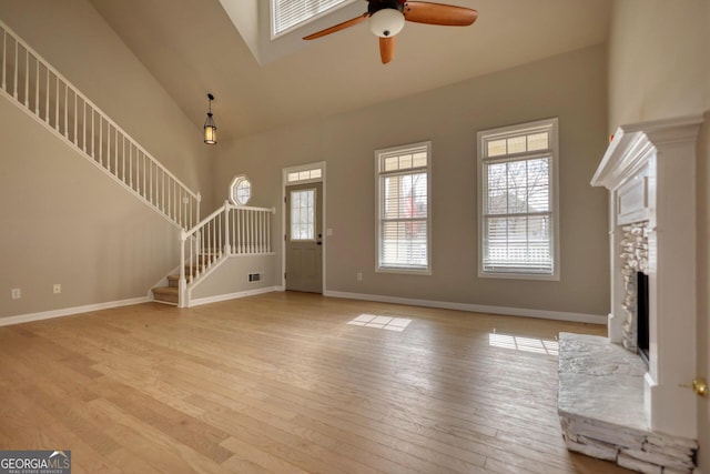 unfurnished living room with a fireplace, a towering ceiling, light hardwood / wood-style flooring, and ceiling fan