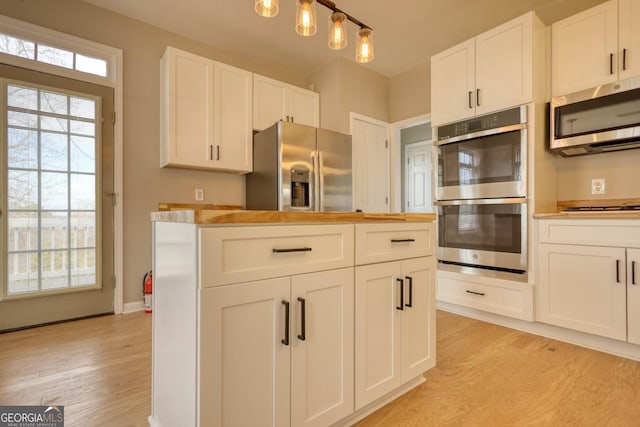 kitchen featuring stainless steel appliances, white cabinetry, pendant lighting, and light hardwood / wood-style floors