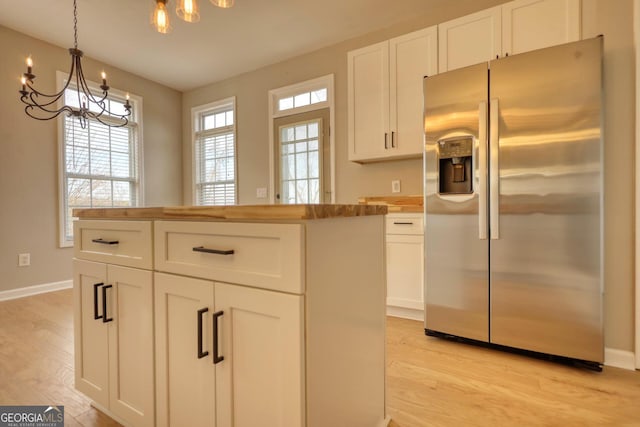 kitchen featuring white cabinetry, wooden counters, stainless steel fridge, and hanging light fixtures