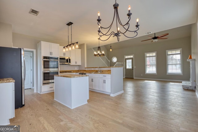 kitchen featuring white cabinetry, decorative light fixtures, light wood-type flooring, and appliances with stainless steel finishes